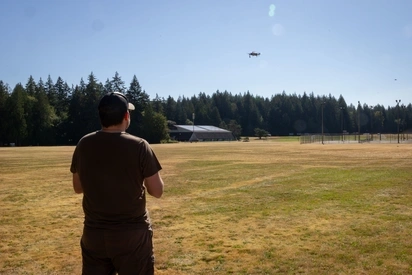 Over the shoulder picture of a student flying a drone over a field