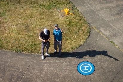 A student and instructor look up at the drone they are piloting
